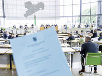 blaue Tagesordnung (unscharf), im Hintergrund Plenarsaal mit Abgeordneten