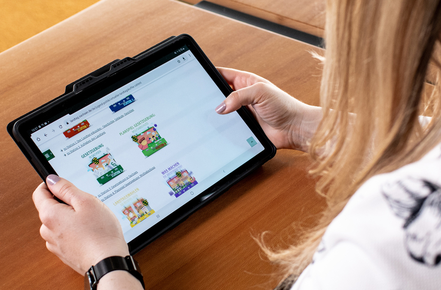 Hände mit Tablet, auf dem die Seite mit den Virtuellen Landtagskoffern geöffne ist