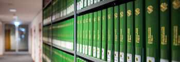 In einem Regal stehen viele Bücher mit dem gleichen grünen Buchrücken und goldener eingeprägter Schrift.