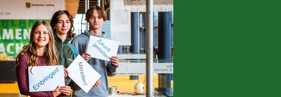 Jugendlche halten Zettel mit den Aufforderungen Einbringen, Mitreden, Zukunft gestalten in die Kamera
