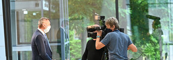 Ein Mann mit Mund-Nasen-Schutz wird von einem Kamerateam gefilmt.