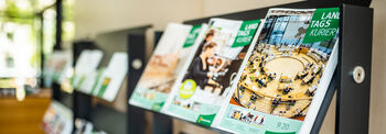 Im Vordergrund liegen Zeitschriften des Landtagskuriers auf einem Regal, im Hintergrund erkennt man weitere Regale mit Publikationen darauf.