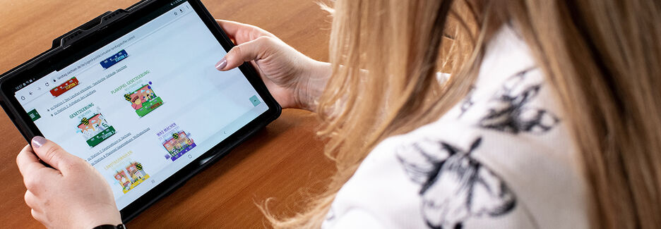 Hände mit Tablet, auf dem die Seite mit den virtuellen Landtagskoffern aufgerufen ist