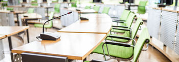Unbesetzte grüne Stühle stehen vor Tischen mit Mikrofonen darauf. 