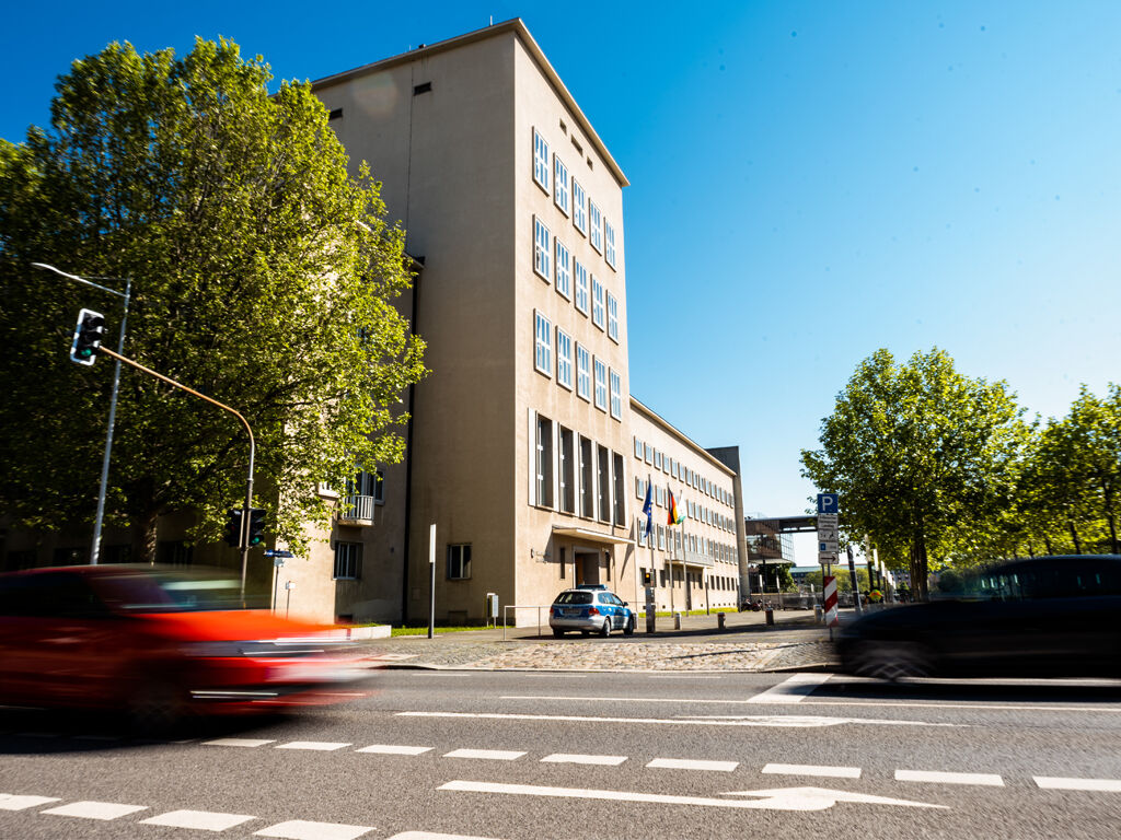 Vor dem Eingang des Landtag-Altbaus fahren ein rotes und ein schwarzes Auto vorbei.