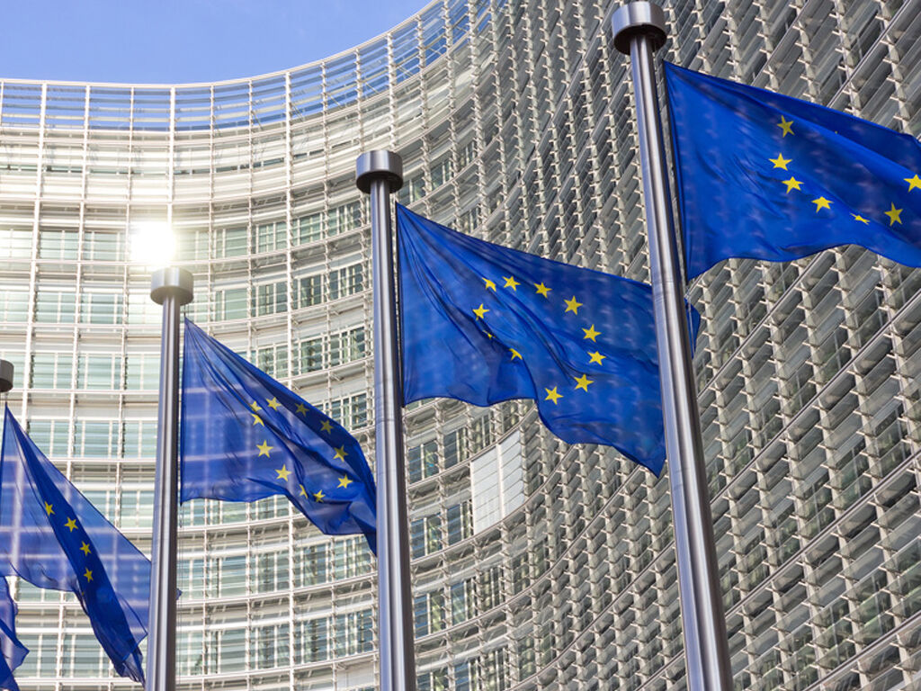Vier Europaflaggen wehen an Masten vor einem grauen Gebäude