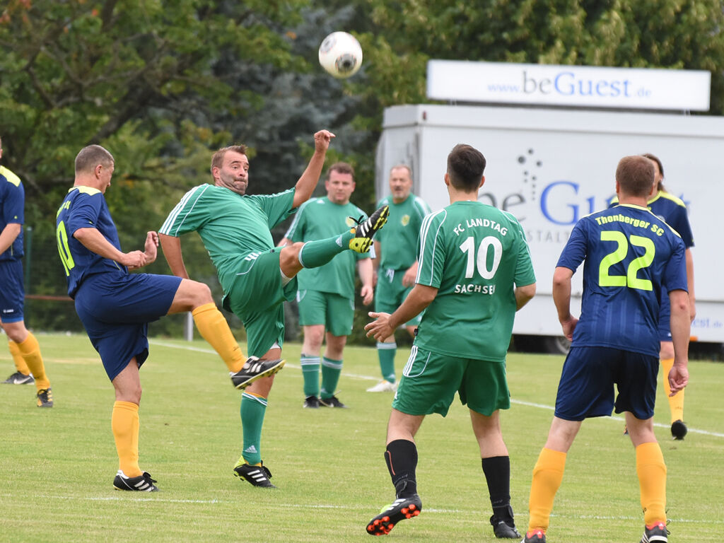Mehrere Fußballspieler in grünen und blauen Trikots spielen gemeinsam auf einem Rasen.
