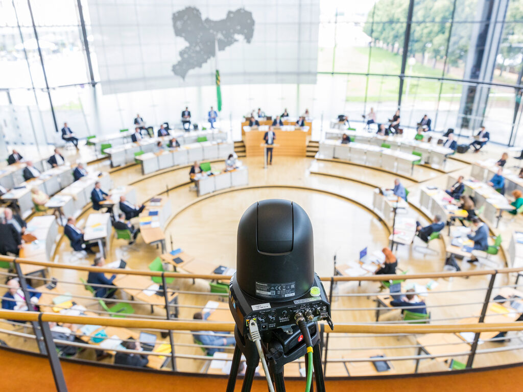 Eine kleine Übertragungskamera steht auf der Besuchertribüne mit Blick auf das vollbesetzte Plenum.