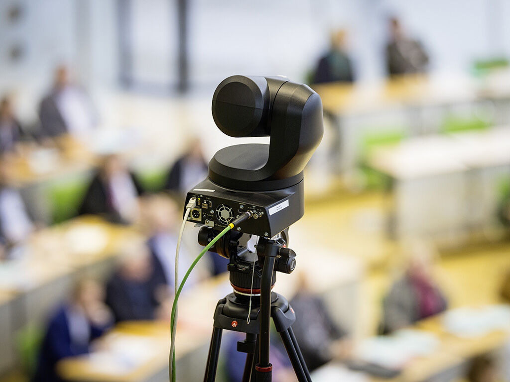 Eine kleine Übertragungskamera steht auf der Besuchertribüne mit Blick auf das vollbesetzte Plenum.