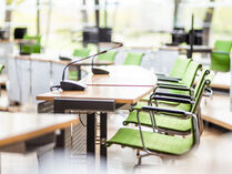 Im Plenarsaal stehen leere grüne Stühle an Tischen, auf denen kleine Mikrofone stehen.