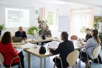 Viele Menschen sitzen in einem Raum an einem Tisch zu einem gemeinsamen Termin.