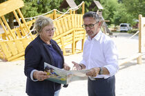 Sören Voigt schaut mit Sylvia Ott eine Broschüre an. Im Hintergrund ist ein Spielplatz mit Holzschiff zu sehen.