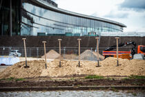 Sechs Spaten stecken nebeneinander in einem Sandhaufen. Im Hintergrund ist das Kongresszentrum zu sehen.