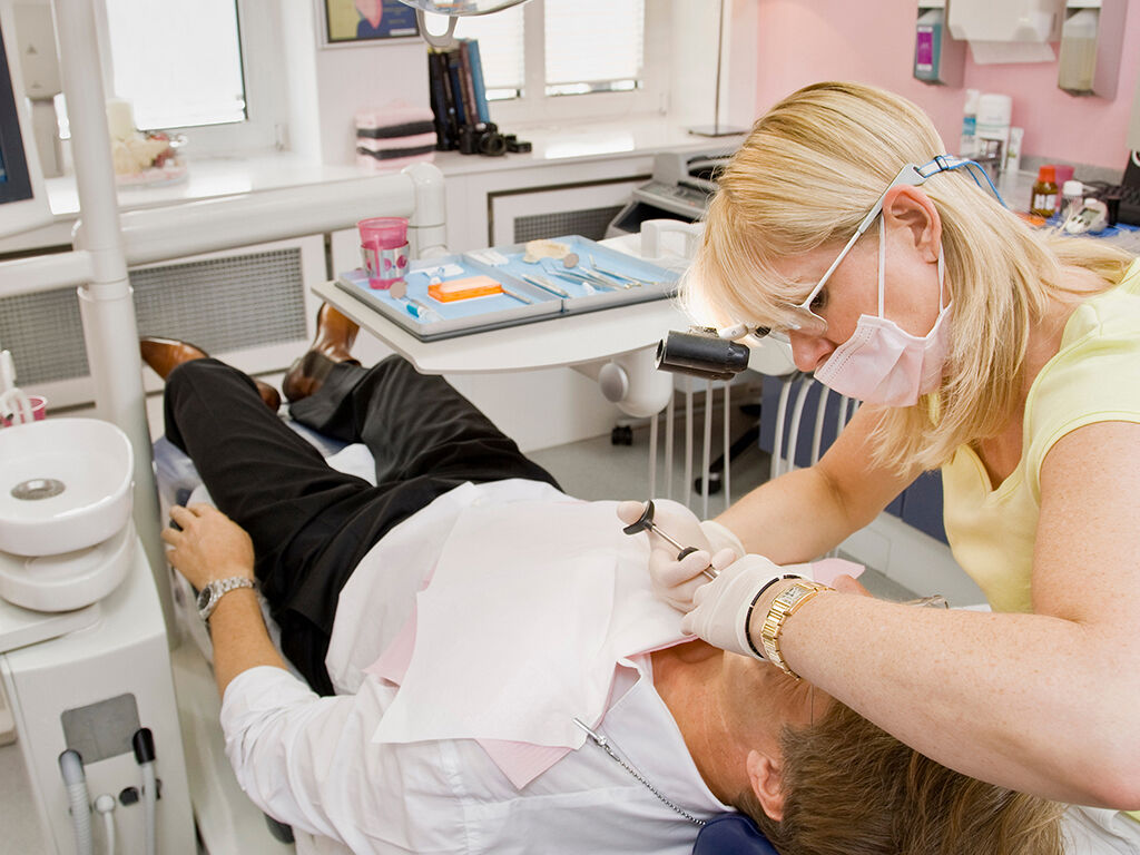 Patient liegt mit geöffnetem Mund auf einem Behandlungsstuhl bei einer Zahnärztin.