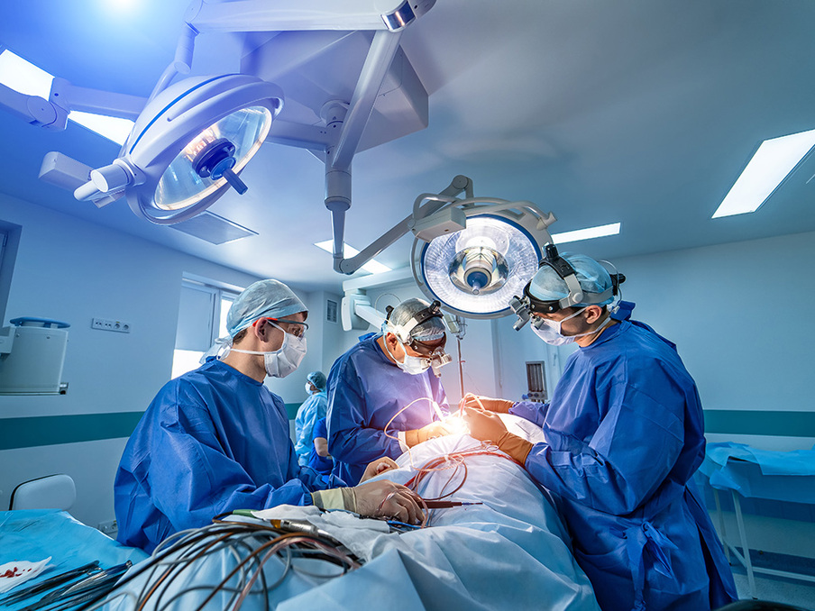 Mehrere Menschen stehen in Operationskleidung um einen Operationstisch und operieren eine Person.