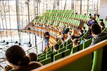 Auf der Besuchertribüne sitzen Schülerinnen und Schüler. Vor ihnen an der Brüstung steht eine Gruppenführerin.