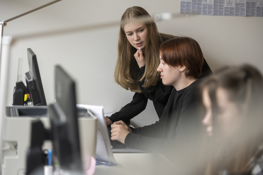 Eine Auszubildende des Landtags erklärt einem Schüler die Aufgabe, die er an einem PC zu lösen hat.