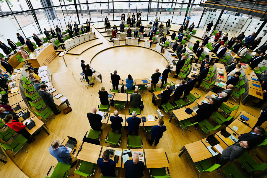 Blick von oben in den Plenarsaal, wo sich die Abgeordneten von ihren Plätzen erhoben haben zu einer Schweigeminute.