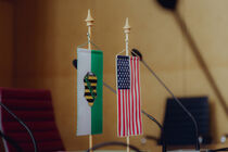 Wimpel von Sachsen und den USA stehen nebeneinander auf einem Tisch.