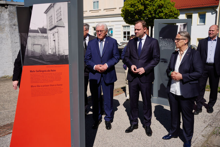 Bundespräsident und Landtagspräsident vor Gedenkstele mit Bildern der Heimkinder