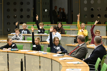 Die Schüler dürfen auf den Sitzen der Abgeordneten Platz nehmen und jeder merkt, dass großer Redebedarf besteht: Viele Schüler heben die Hände und möchten mitdiskutieren 