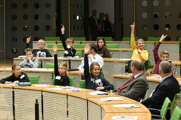 Die Schüler dürfen auf den Sitzen der Abgeordneten Platz nehmen und jeder merkt, dass großer Redebedarf besteht: Viele Schüler heben die Hände und möchten mitdiskutieren 