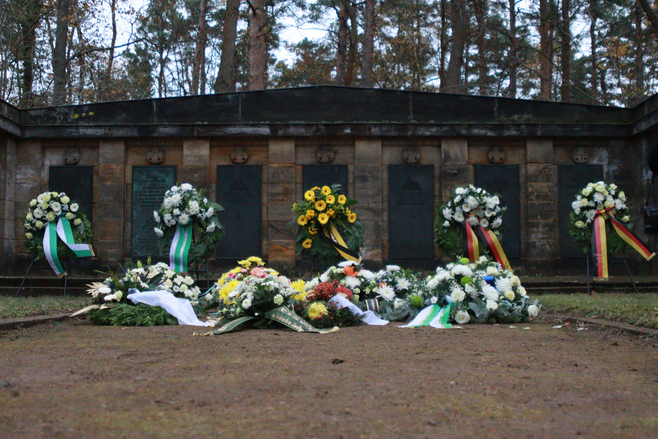 Vier Kränze und Blumen liegen auf dem Boden