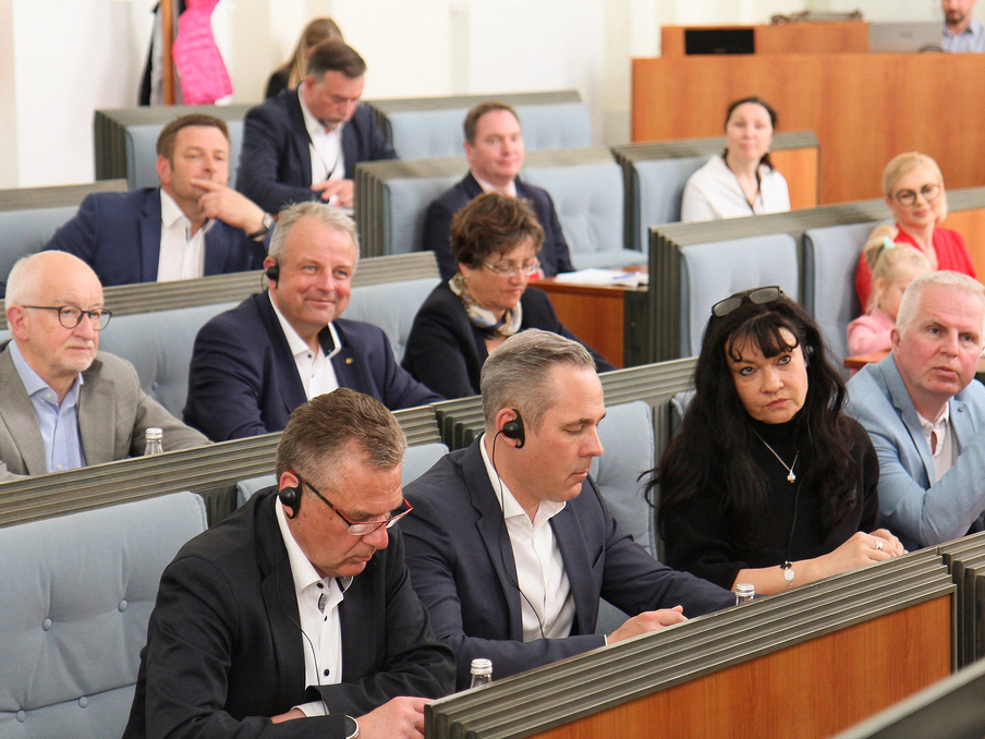 Delegation des Wirtschaftsausschusses sitzt in Reihen in einem Saal und verfolgt eine Sitzung.