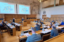 Die Delegation sitzt im Sitzungssaal des Grossen Rates Bern. An der Wand ist eine Präsentation zu den Strukturen der Schweiz zu sehen.