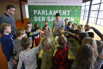Viele Kinder stehen um ein Modell des Landtages herum und zeigen mit den Fingern darauf