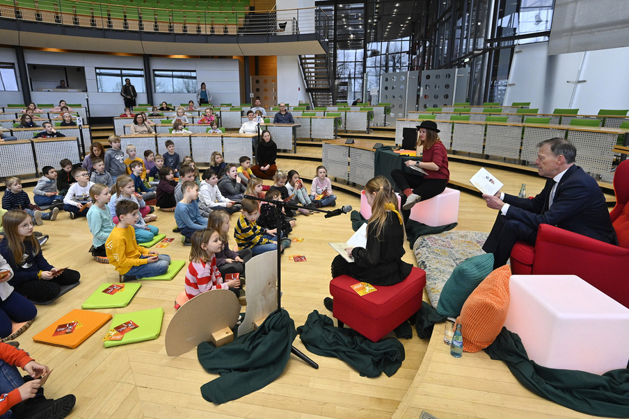 Viele Kinder sitzen auf Kissen im Plenarsaalrund sowie auf den Abgeordnetenstühlen und Landtagspräsident Dr. Matthias Rößler in einem roten Sessel.