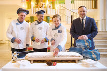 Vertreter des Stollenverbandes in Bäckerkleidung sowie Landtagspräsident Alexander Dierks beim Anschnitt eines großen Stollens.