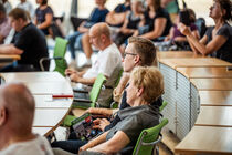 Besucher hören im Plenarsaal auf den Abgeordnetenstühlen zu.