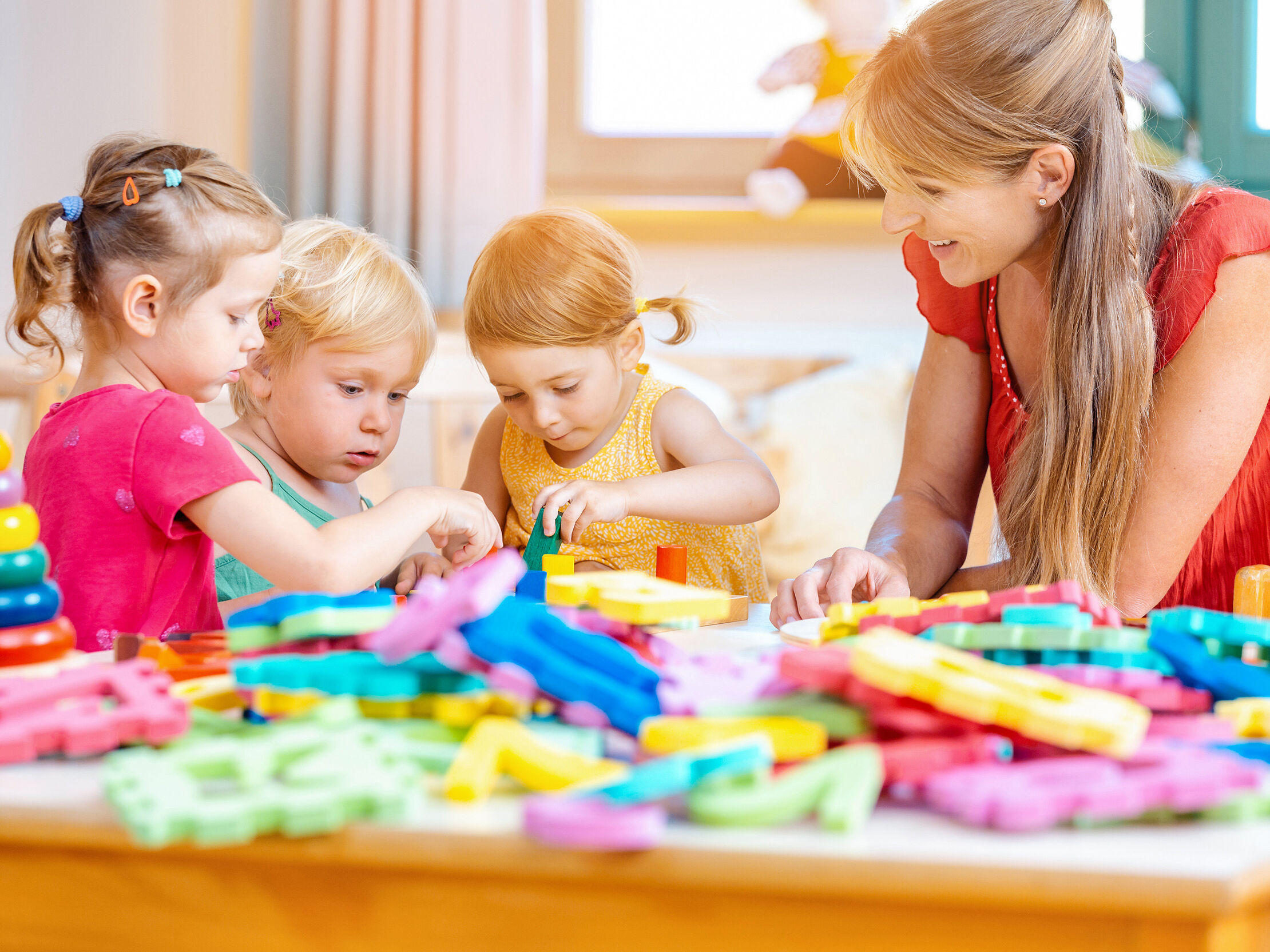 Kitakinder und Erzieherin spielen mit bunten Puzzleteilen.